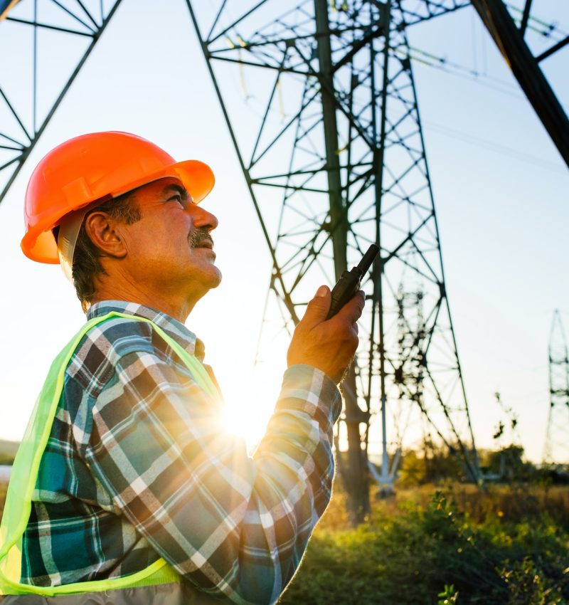 Electrician talking on portable radio device near high voltage tower