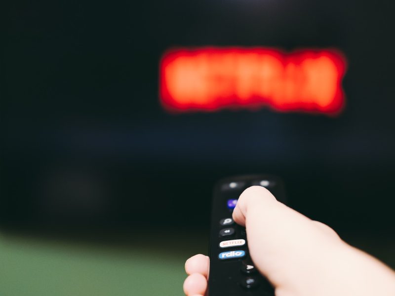 Woman using remote control to switch streaming service on television